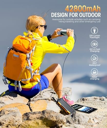 Person using a portable solar charger on a rocky outdoor setting.